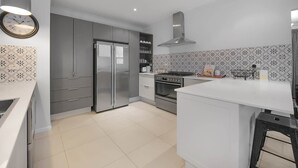 Een moderne keuken met grijze kastjes, een roestvrijstalen koelkast, een oven en een wit aanrecht.