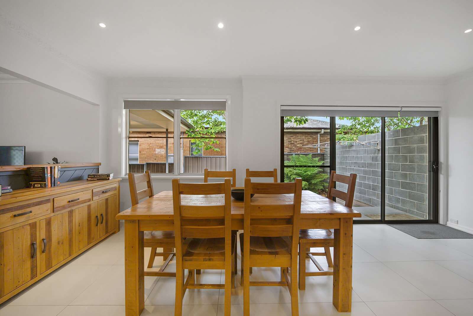 A modern kitchen with a dining area, wooden cabinets, and a sliding glass door leading to a backyard.