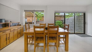 Een moderne keuken met een eethoek, houten keukenkastjes en een schuifdeur naar een achtertuin.