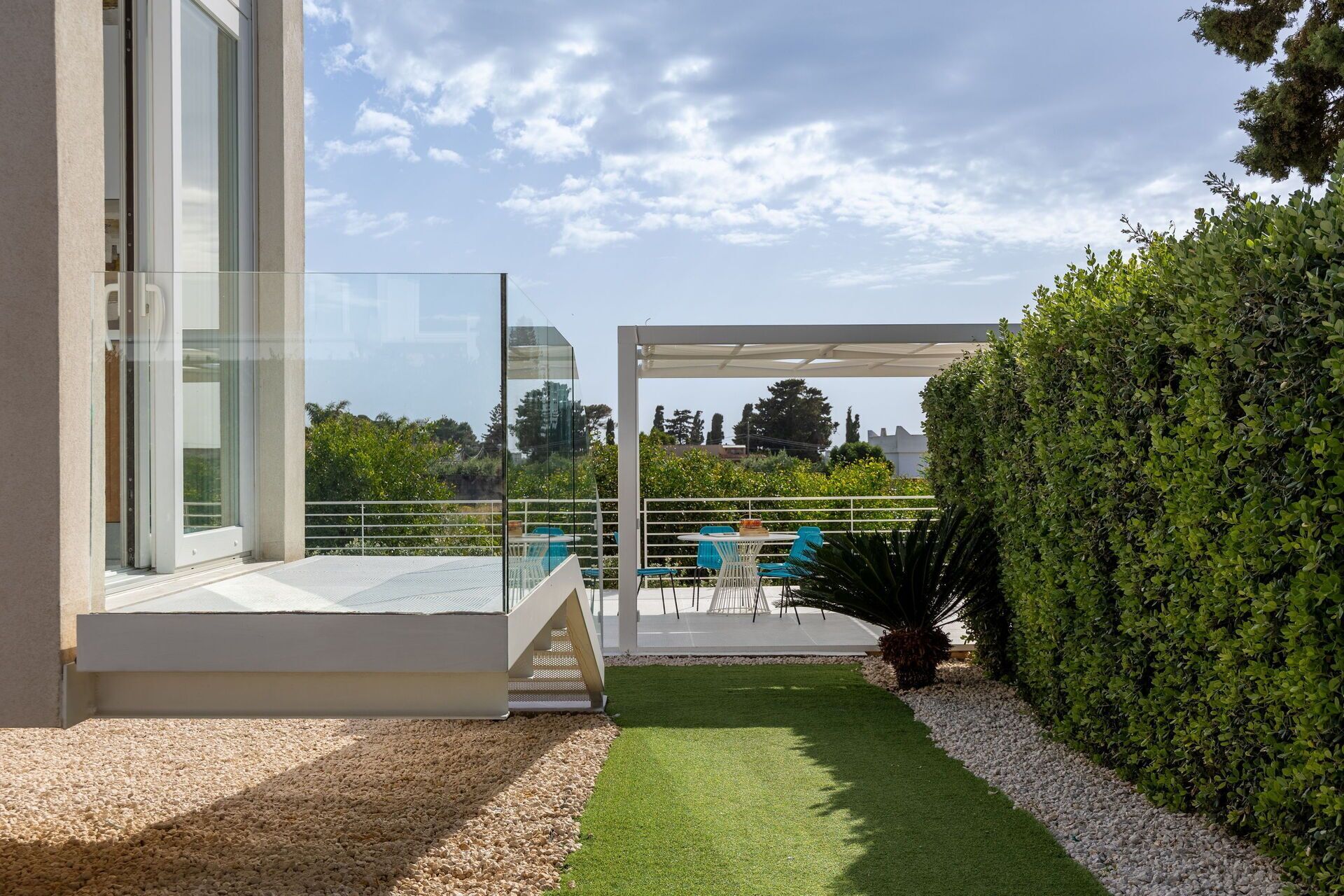 A modern outdoor patio with a glass door, a white pergola, and a well-maintained lawn.