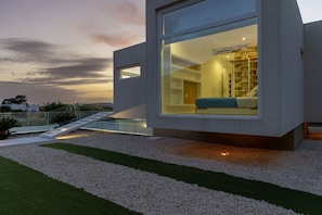 A modern building with a large glass window, a staircase, and a view of a bedroom with a bed and a nightstand.