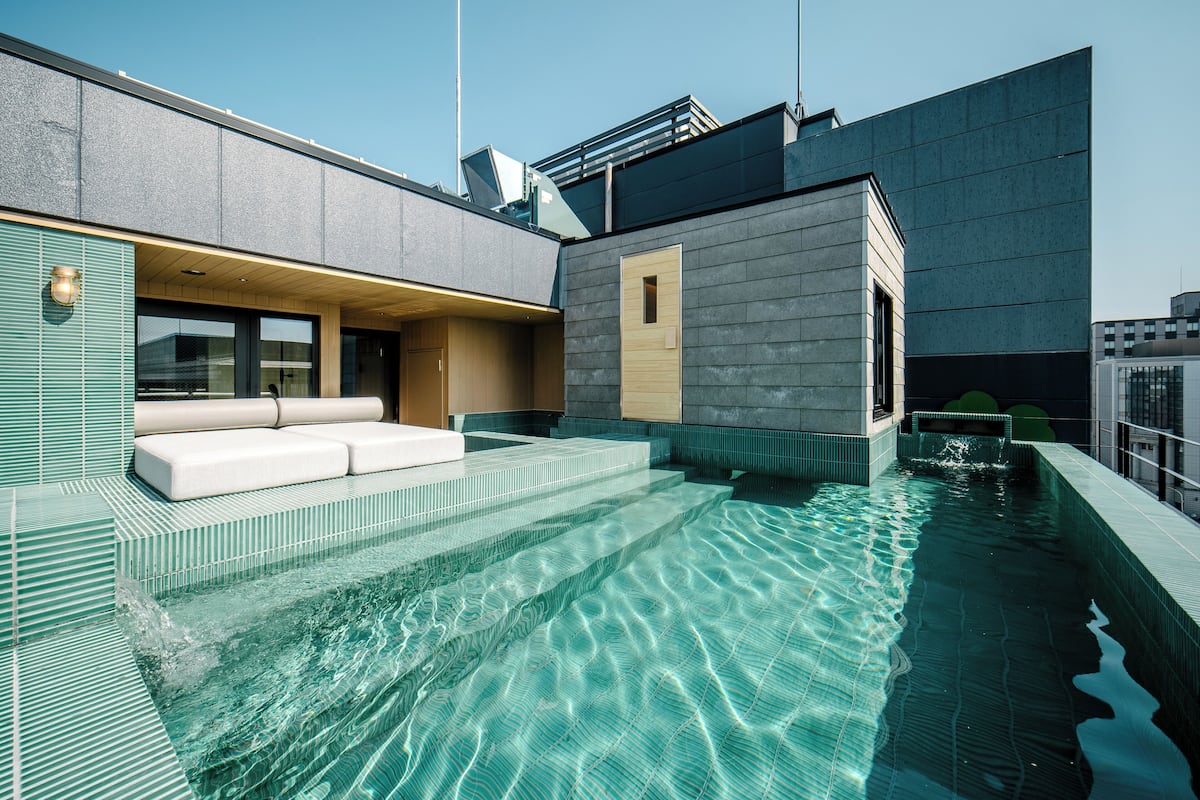 A rooftop infinity pool with a modern design, a seating area with a sofa and a small table, and a view of the city skyline.