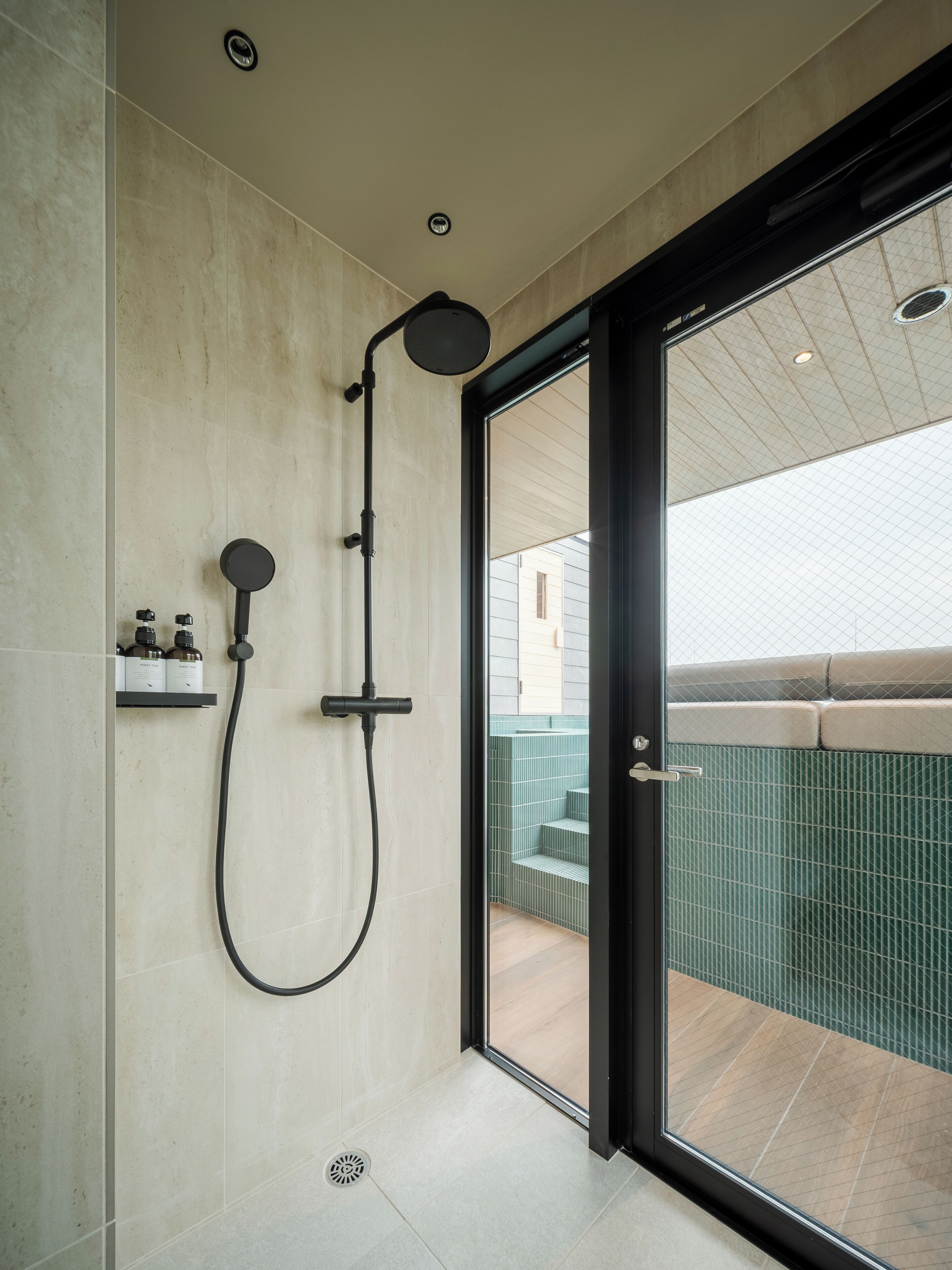 A modern bathroom with a glass shower enclosure, a built-in shelf with toiletries, and a view of the outdoor area.