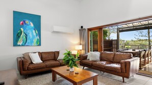 A living room with two brown leather sofas, a wooden coffee table, a potted plant, and a large abstract painting on the wall.