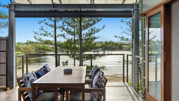 An outdoor patio with a table and chairs, a pergola with string lights, a view of a body of water, and a wooden deck.