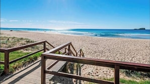 A wooden boardwalk leading to a sandy beach with a clear blue sky and the sun shining brightly.