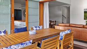 A modern interior with a wooden dining table, chairs, a sofa, and a view of a room with a staircase.