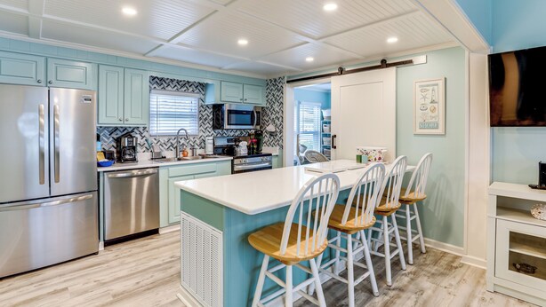 A kitchen with a central island, bar stools, stainless steel appliances, and a herringbone-patterned backsplash. - Walk to Shore! Surfside Beach Gem w/ Game Courts (Surfside Beach)