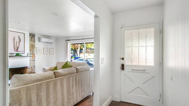 Una habitación con sofá color beige, una puerta blanca con ventanal texturizado y una pared de piedra con obras de arte.