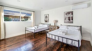 Habitación de hotel con dos camas individuales, una mesita de noche de madera, una ventana con vistas a un edificio y un aire acondicionado instalado en la pared.