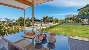A dining table with food and drinks on a deck with a view of a road and greenery. - Innisfree Marahau Retreat (Kaiteriteri - Mārahau)