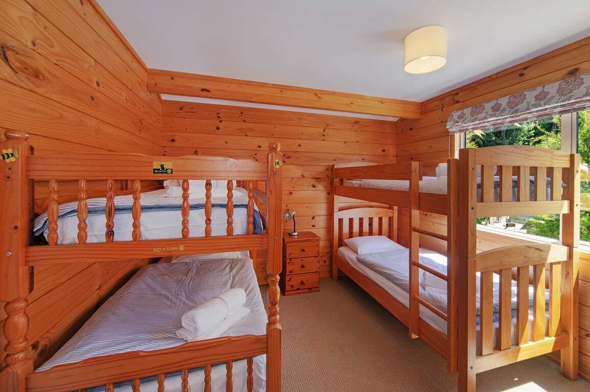 Une chambre dans un chalet en bois, avec des lits superposés, une petite commode en bois et une fenêtre donnant sur un paysage verdoyant.
