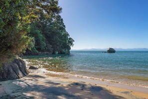 A beach with clear water, a large rock formation, and a mountain range in the distance. - Innisfree Marahau Retreat (Kaiteriteri - Mārahau)