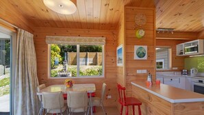 A wooden cabin with a dining area, kitchen, and large windows. - Innisfree Marahau Retreat (Kaiteriteri - Mārahau)