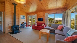 A cozy cabin interior with a wooden interior, a fireplace, a sofa, and a television. - Innisfree Marahau Retreat (Kaiteriteri - Mārahau)
