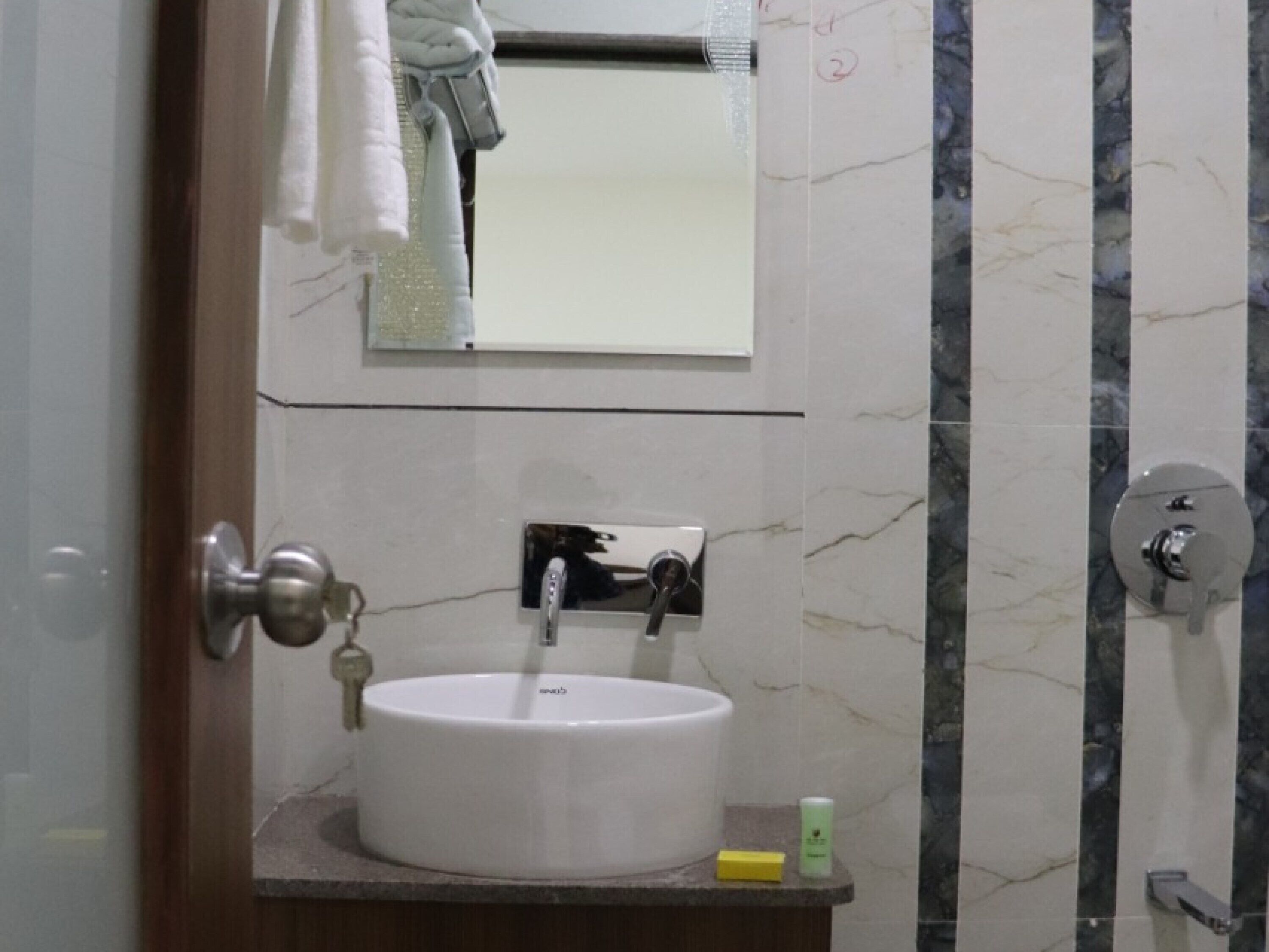 A bathroom with a white sink, a mirror above it, and a shower area with a marble wall.