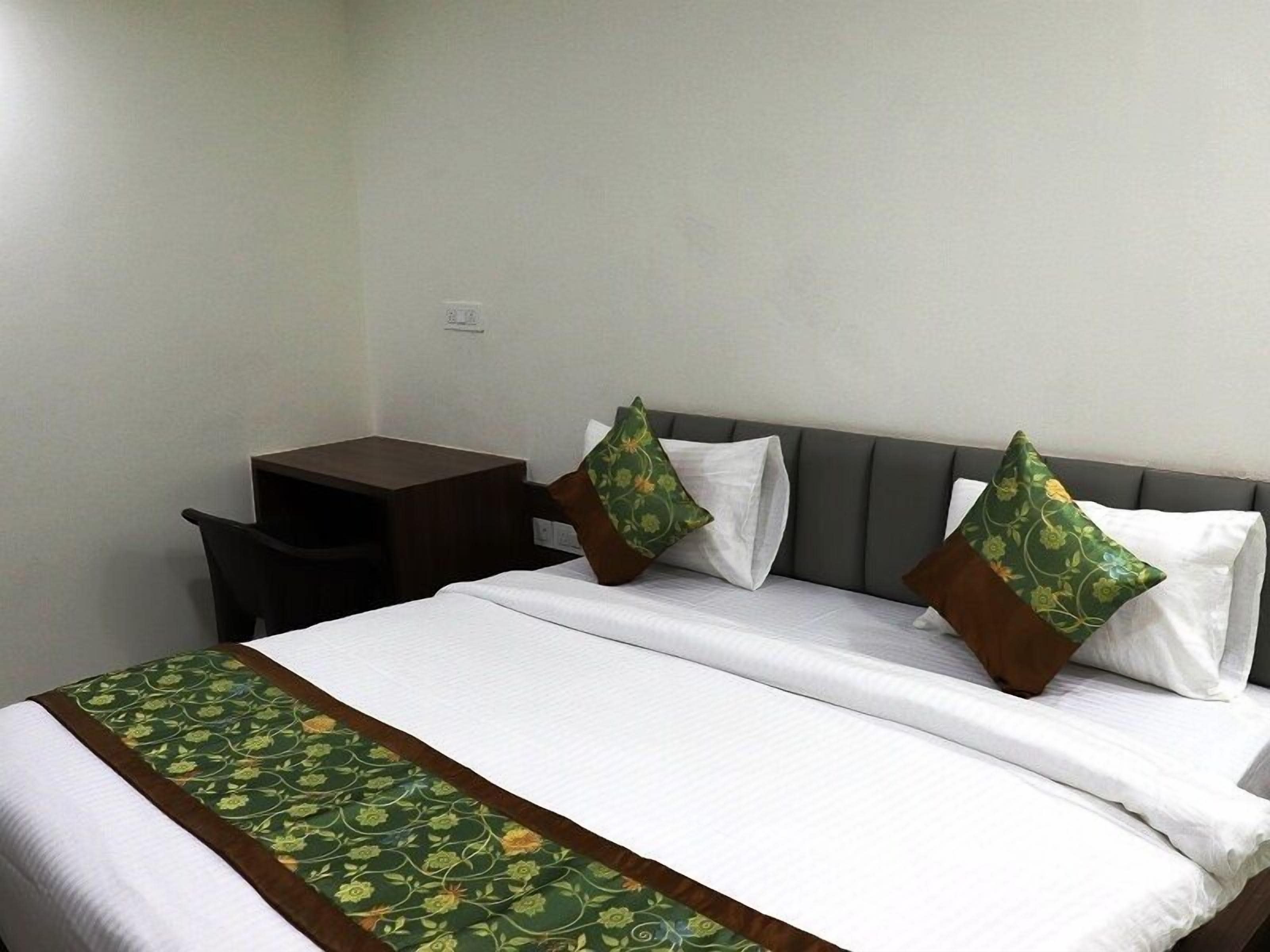 A hotel room with a bed, two pillows, a nightstand, and a desk.