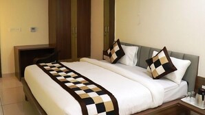 A hotel room with a bed, a desk, a wardrobe, and a wall-mounted fan. - Hotel Kashi Inn (Jodhpur)