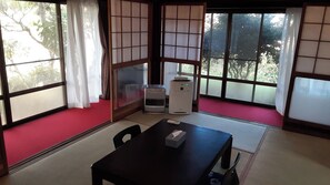 Una habitación japonesa tradicional con suelo de tatami, puertas correderas shoji y una mesa con un control remoto y una caja de pañuelos.