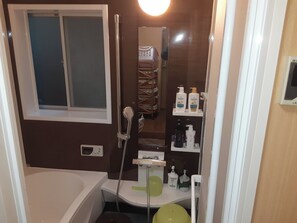 Un baño con bañera, inodoro y ducha. Hay artículos de aseo en un estante.