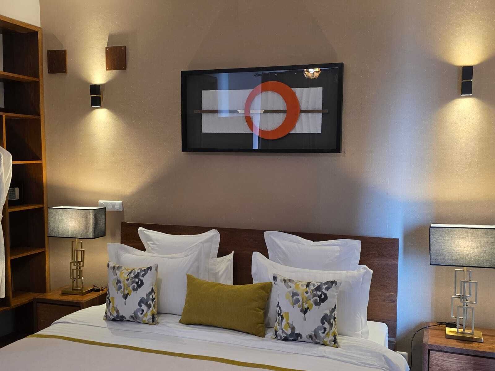 A hotel room with a neatly made bed, two bedside lamps, a wall-mounted artwork, and a wooden wardrobe.