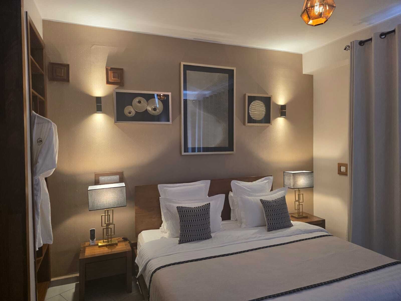 Habitación de hotel con una cama grande, dos mesitas de noche, una lámpara de pared y una luz en el techo.