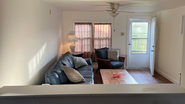 En stue med sofa, bord, stol, loftventilator og dør ud til det fri.