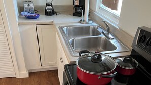 Et lille køkken med komfur, gryder, toaster, blender og kaffemaskine.