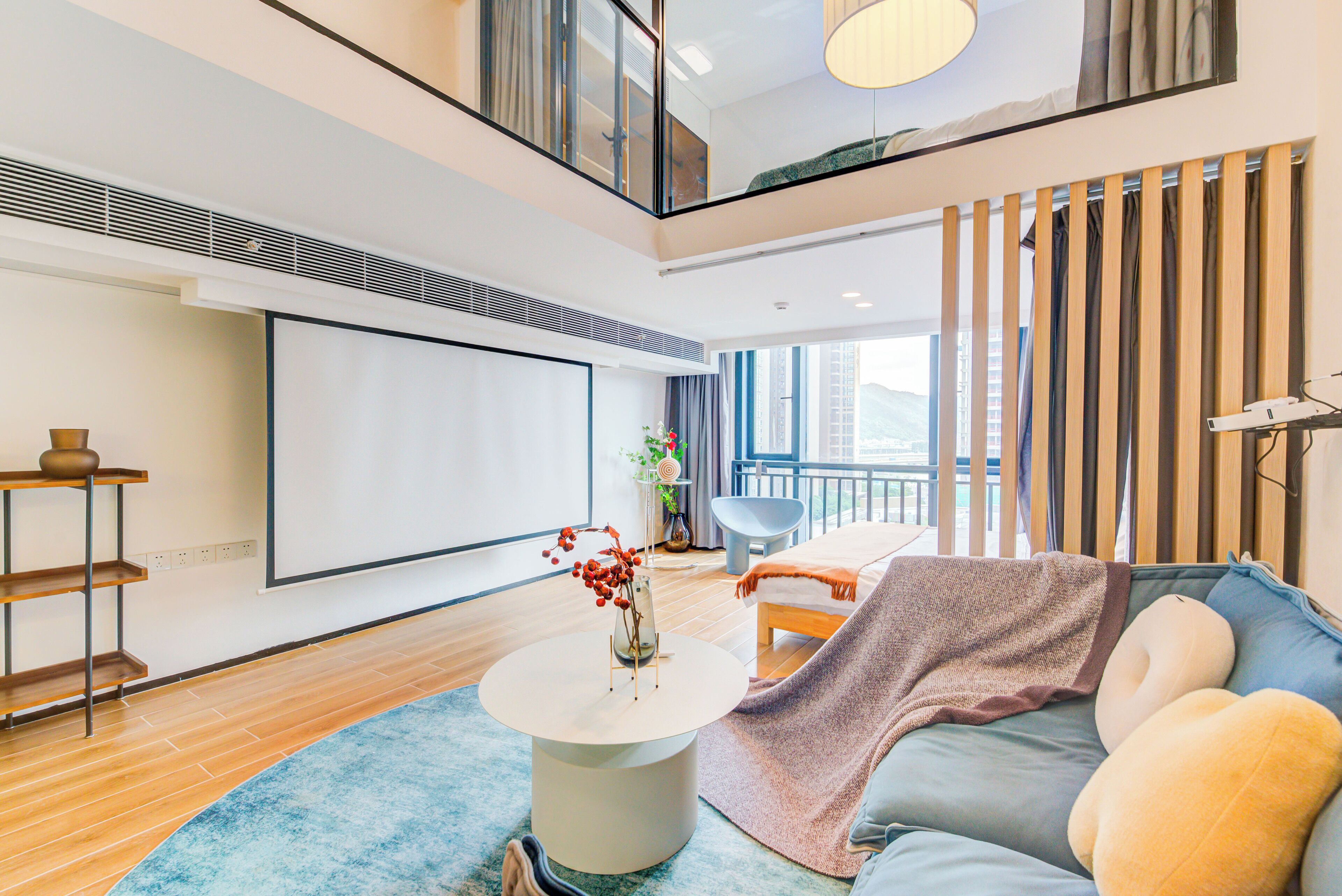 A modern living room with a large flat-screen TV, a round coffee table with a vase, a sofa with cushions, and a view of the city through large windows.