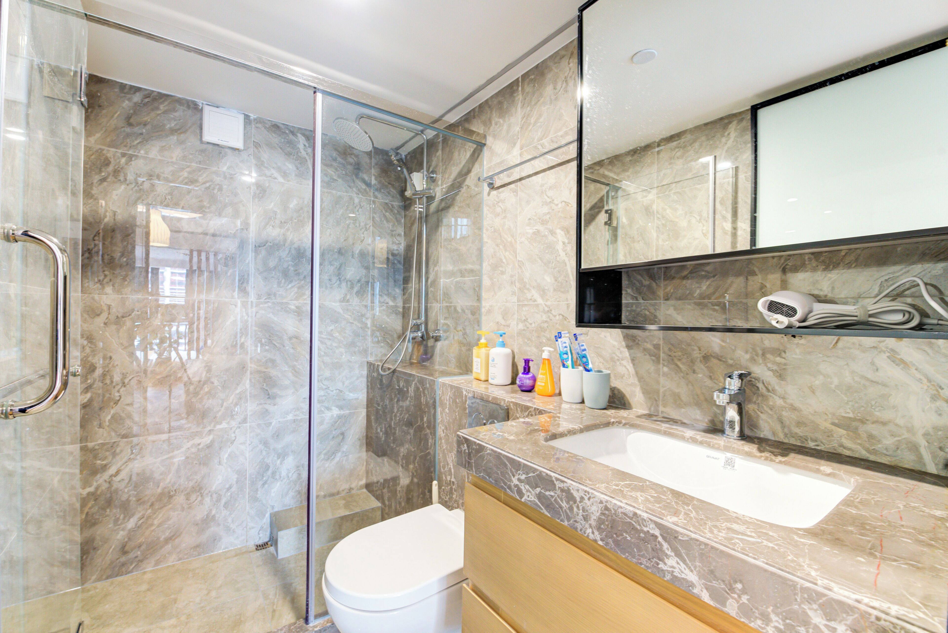 A modern bathroom with a glass-enclosed shower, a white toilet, a marble sink, and a mirror above the sink.