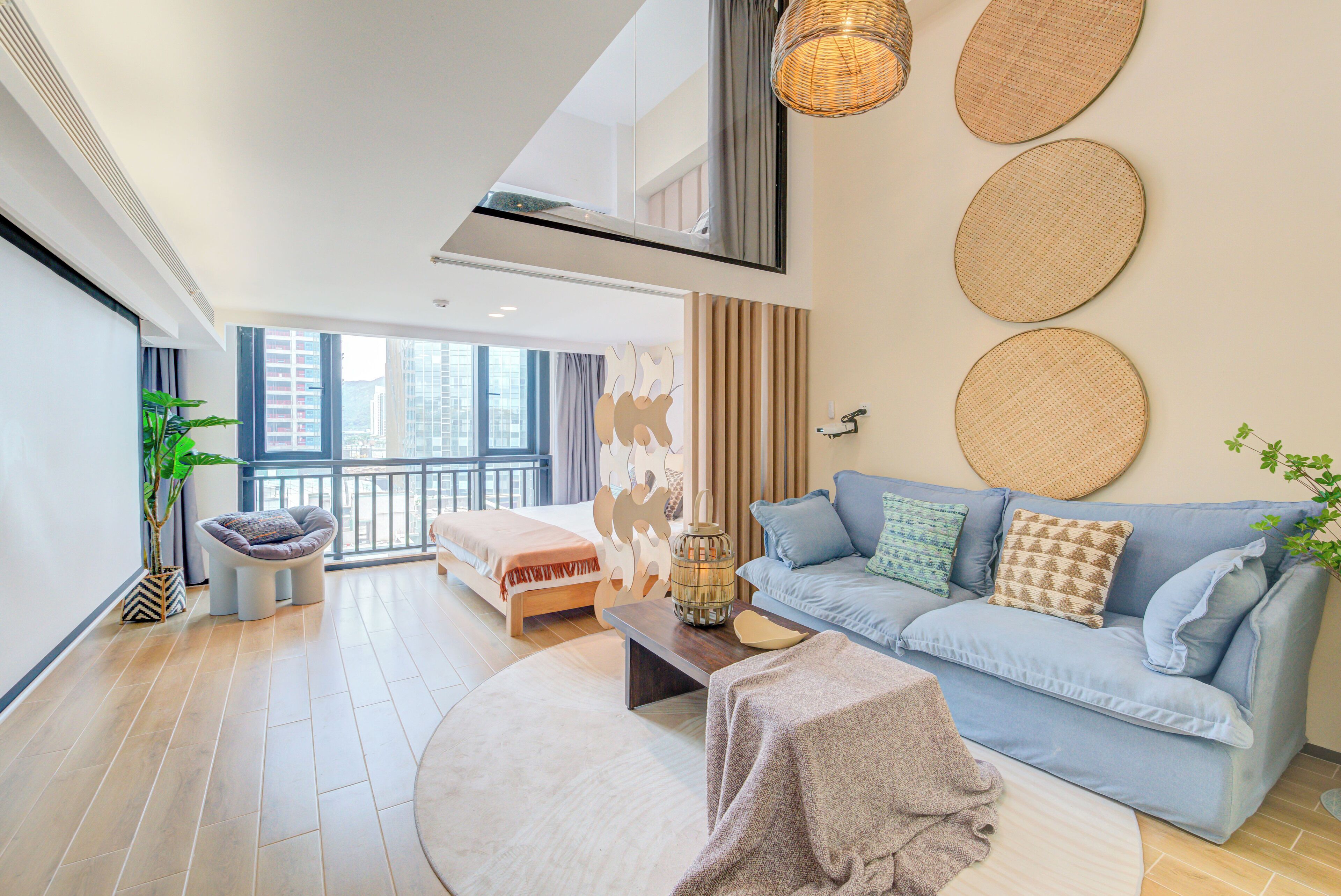 A modern living room with a sofa, a coffee table, and a round rug. There is a large window with a view of buildings outside.