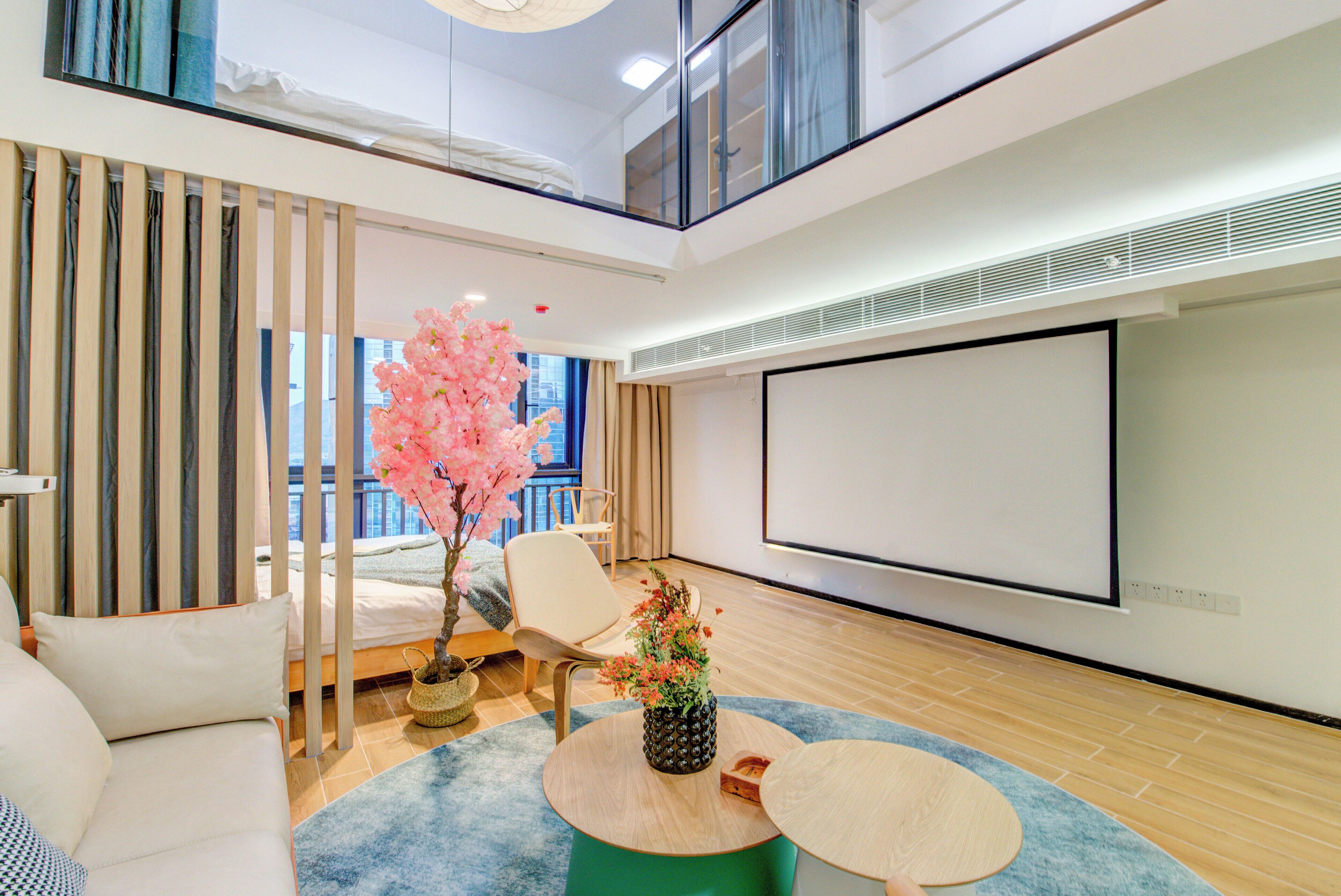Habitación de hotel moderna con cama, zona de estar y una pantalla grande para presentaciones.