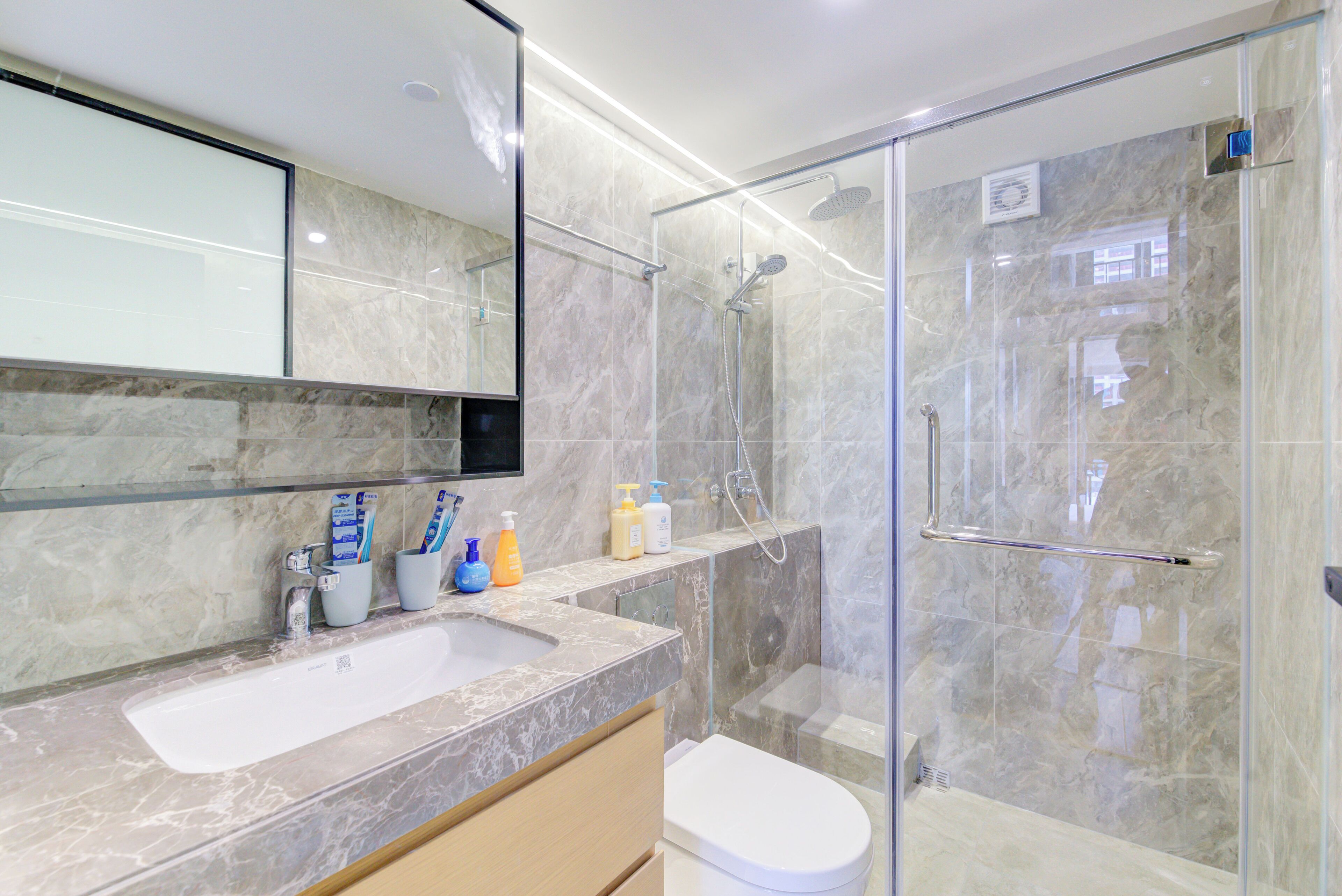 A modern bathroom with a glass-enclosed shower, a marble sink, and a toilet.