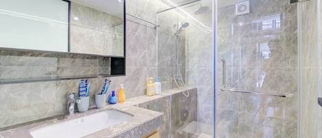 A modern bathroom with a glass-enclosed shower, a marble sink, and a toilet.