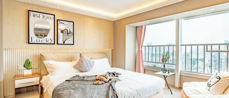Une chambre d’hôtel moderne avec un grand lit, une table de chevet, une petite table avec une plante et une vue sur la ville grâce à de grandes fenêtres.