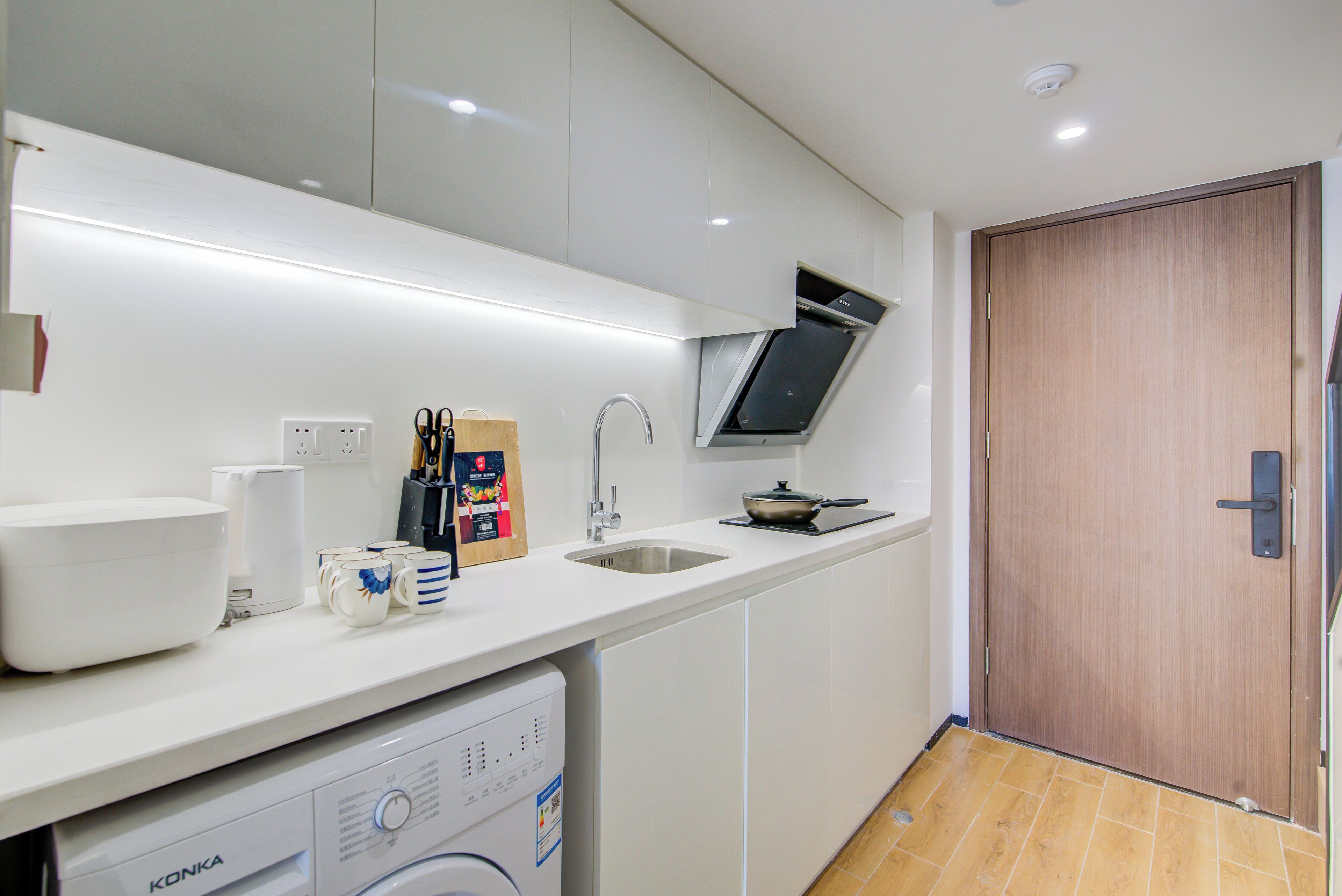 A modern kitchen with a built-in washing machine, a sink, and a wooden door.