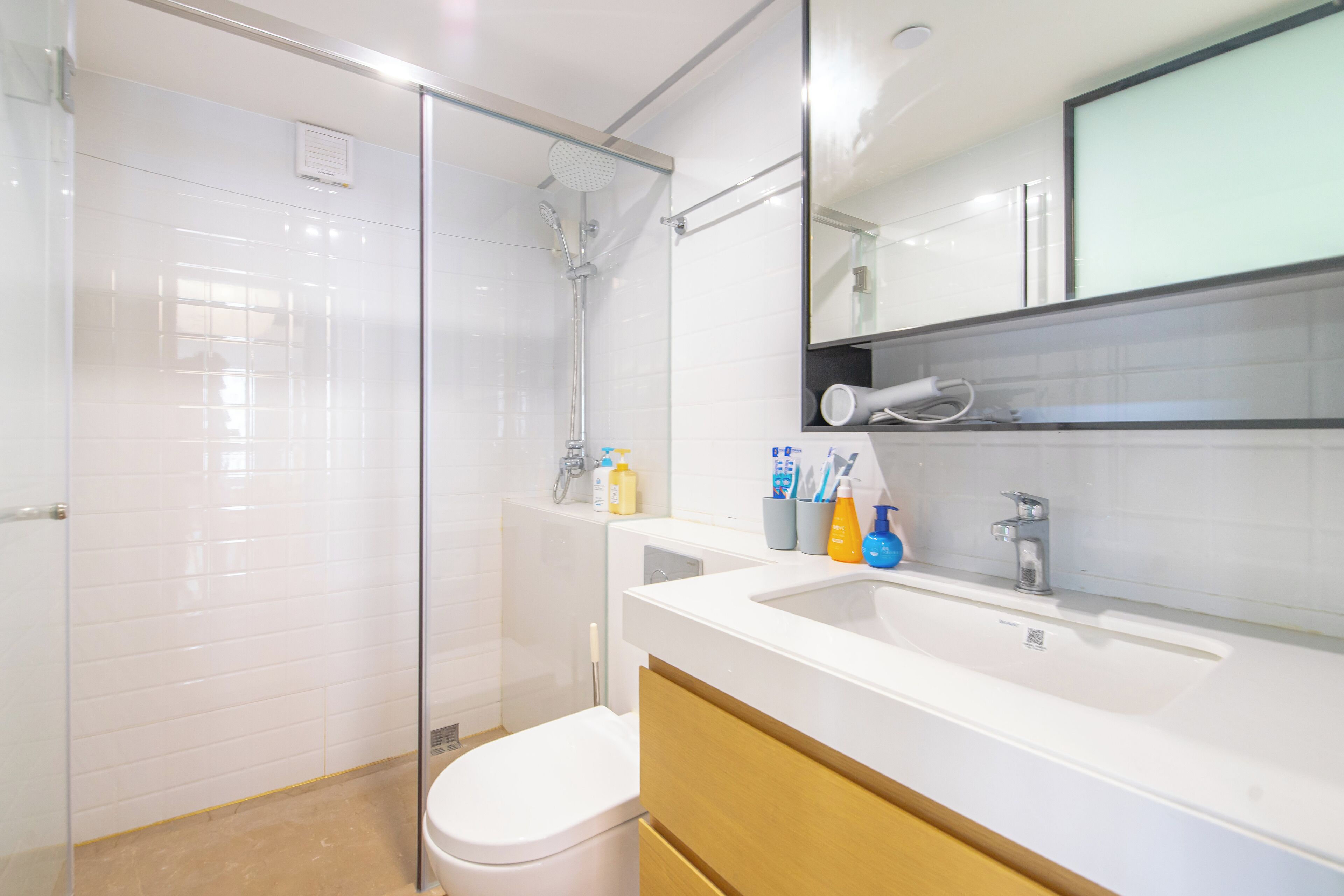 Une salle de bain moderne avec une douche à parois de verre, des toilettes blanches, un lavabo avec des articles de toilette et un miroir au-dessus du lavabo.