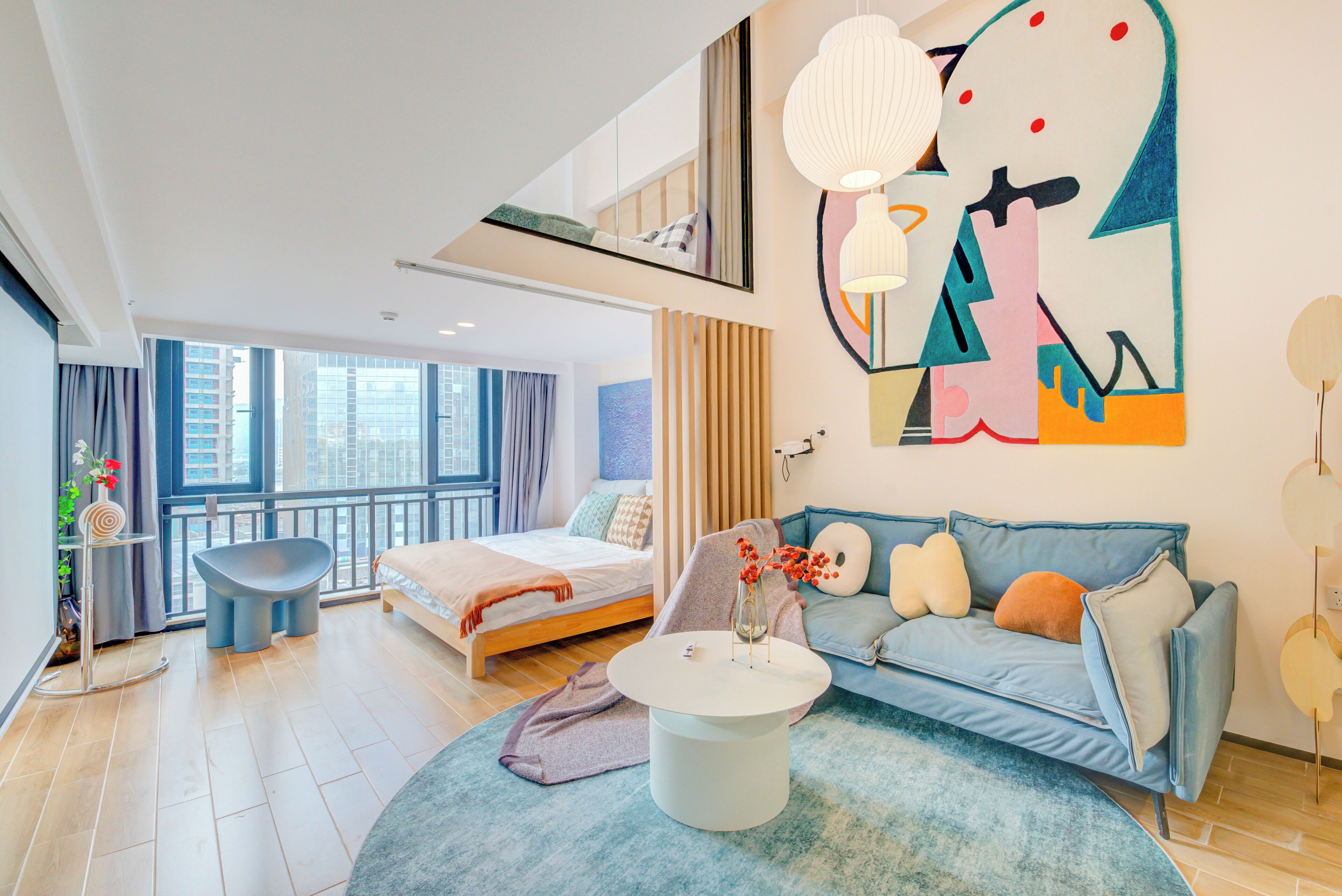 Une chambre d’hôtel moderne avec un grand lit, un canapé, une table basse ronde et un grand tableau abstrait accroché au mur.