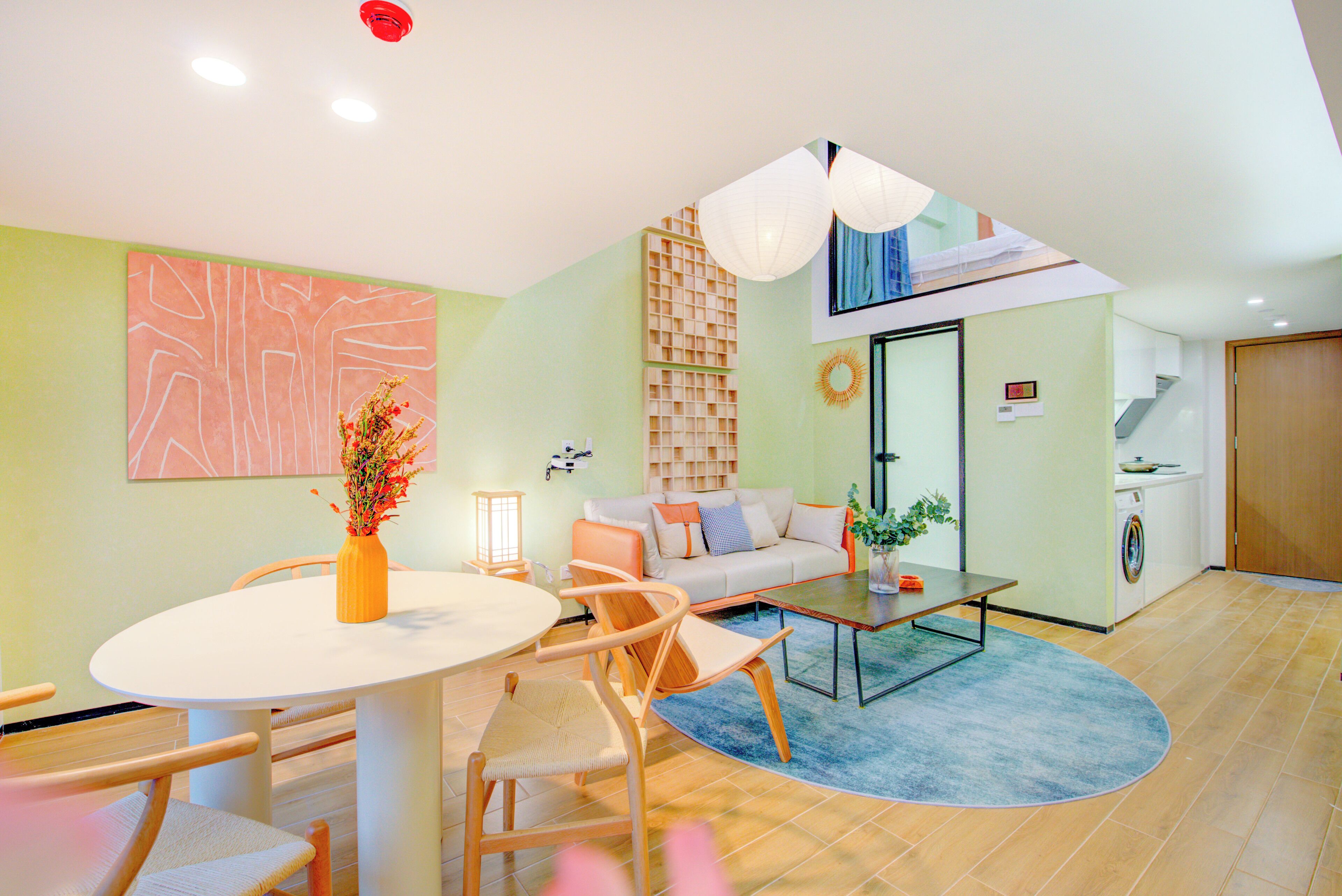 A modern living room with a round dining table, a sofa, and a coffee table. There is a washing machine and a door in the background.