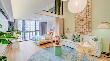 Une chambre d’hôtel moderne avec une grande fenêtre, un lit, un canapé, une table basse et un fauteuil.
