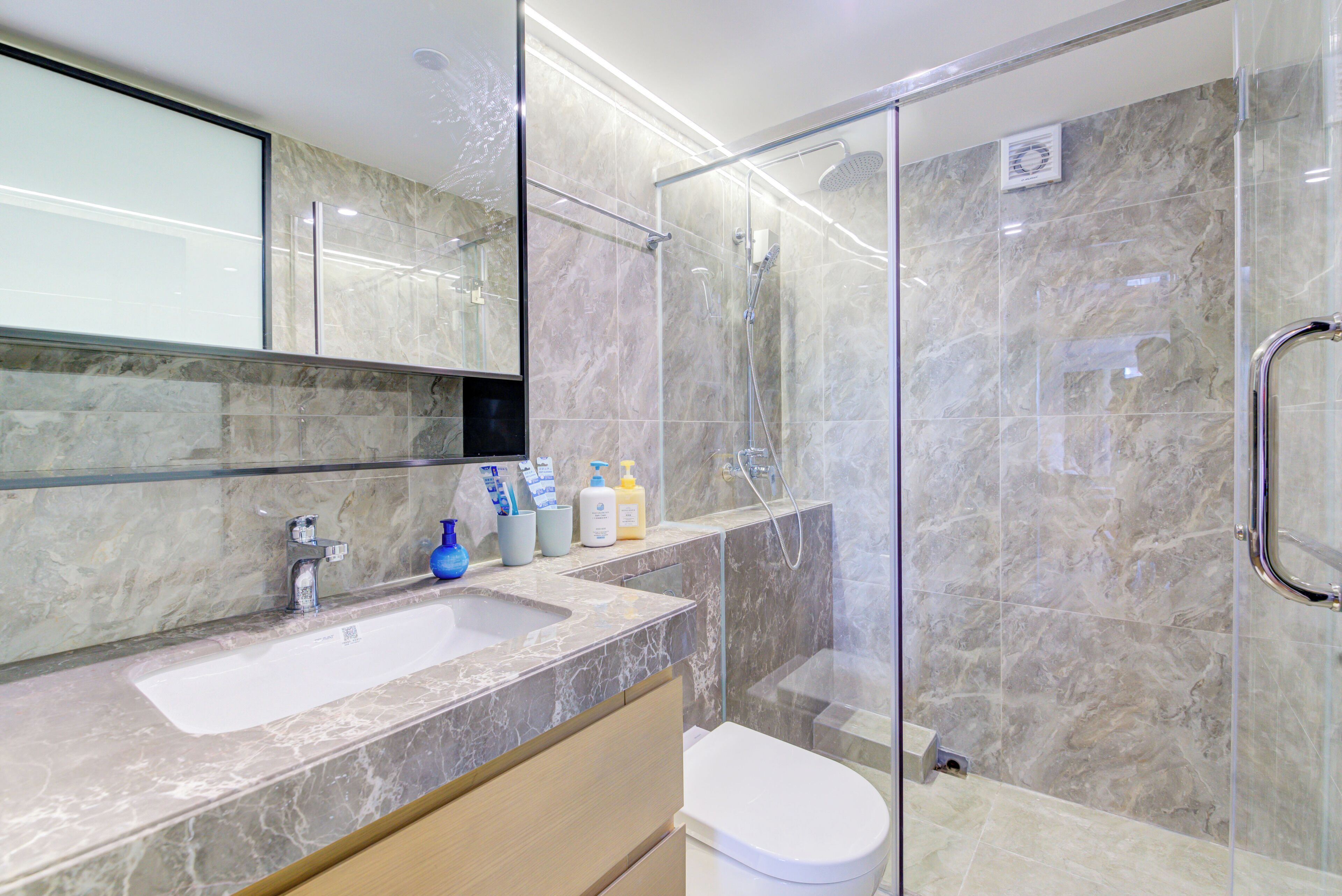 A modern bathroom with a glass-enclosed shower, a marble sink, and a toilet.
