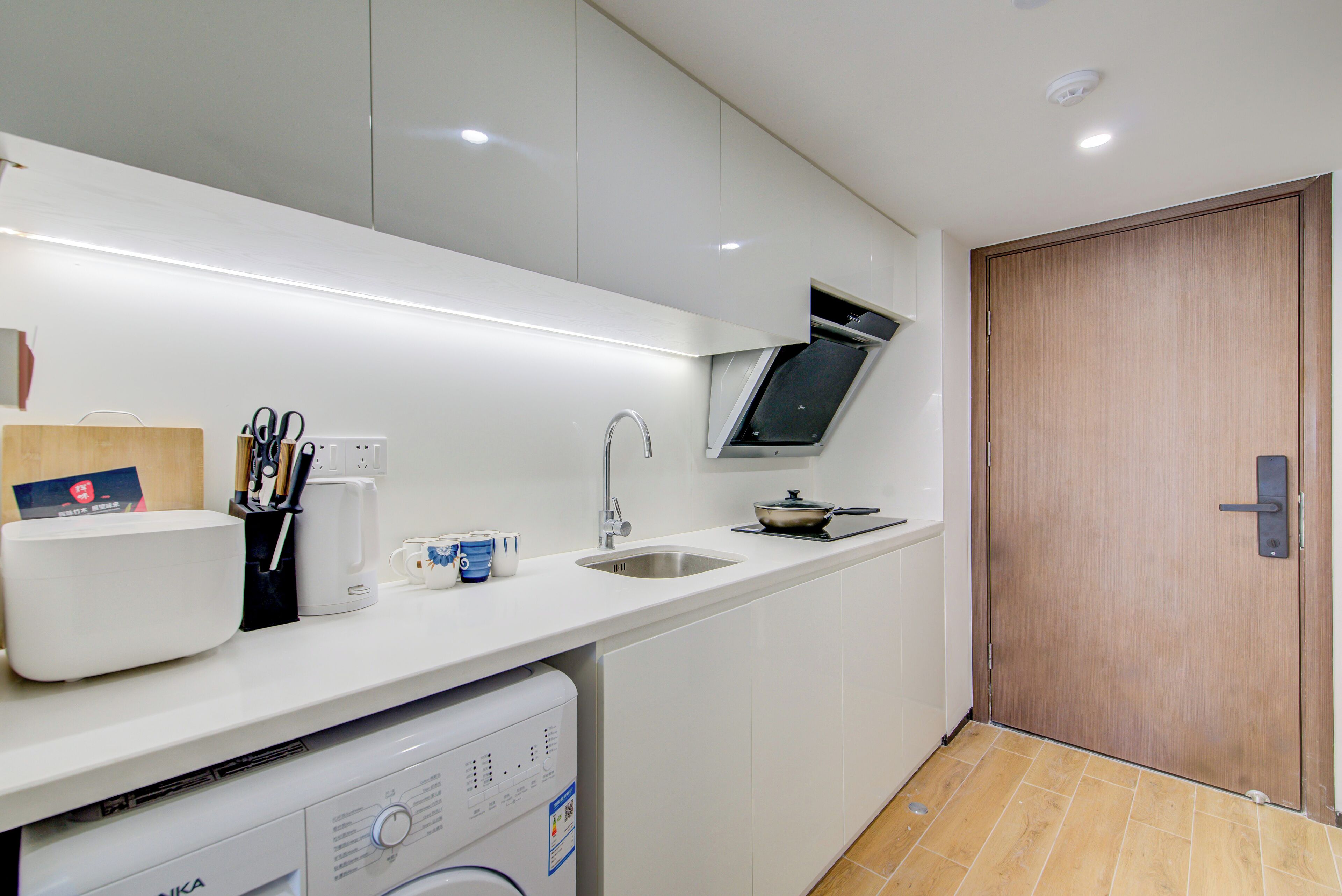 A modern kitchen with a built-in dishwasher, a sink, and a wooden door.
