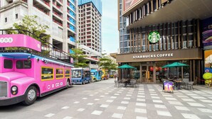 Um ônibus de dois andares rosa estacionado em uma rua da cidade, com um prédio da Starbucks Coffee ao fundo.