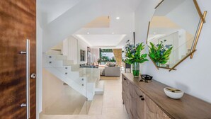A modern interior with a staircase leading to a living area, a wooden counter with a vase, and a large mirror. - VILLA LA PLAGE BY VACATION MARBELLA (Marbella)