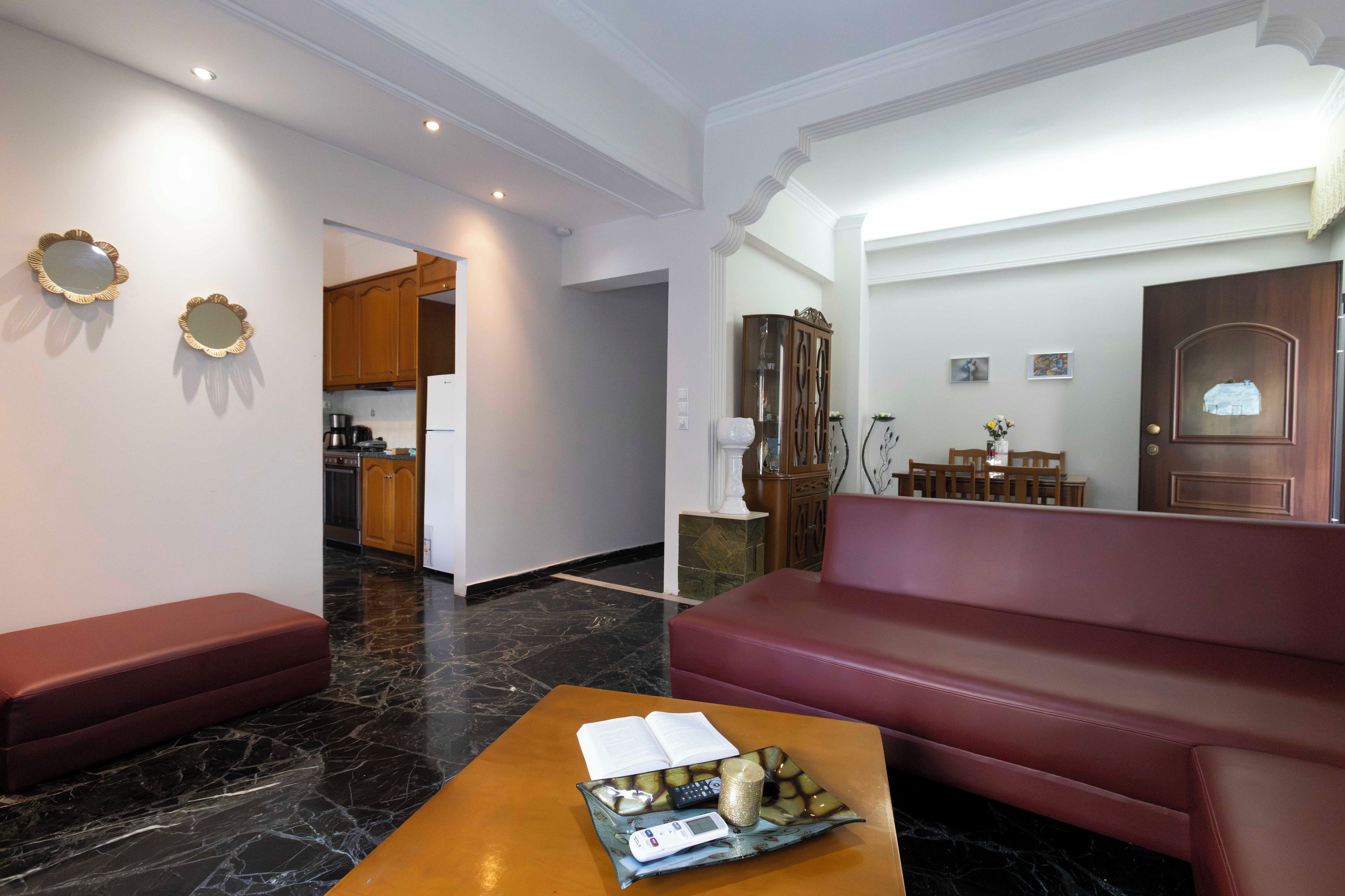 A modern living room with a red sofa, a wooden coffee table with a book and remote control, and a kitchen in the background.