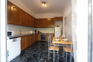 A kitchen with wooden cabinets, a built-in oven, a microwave, and a dining table set for four. - Marias Cozy getaway in Glyfada (Glifada)