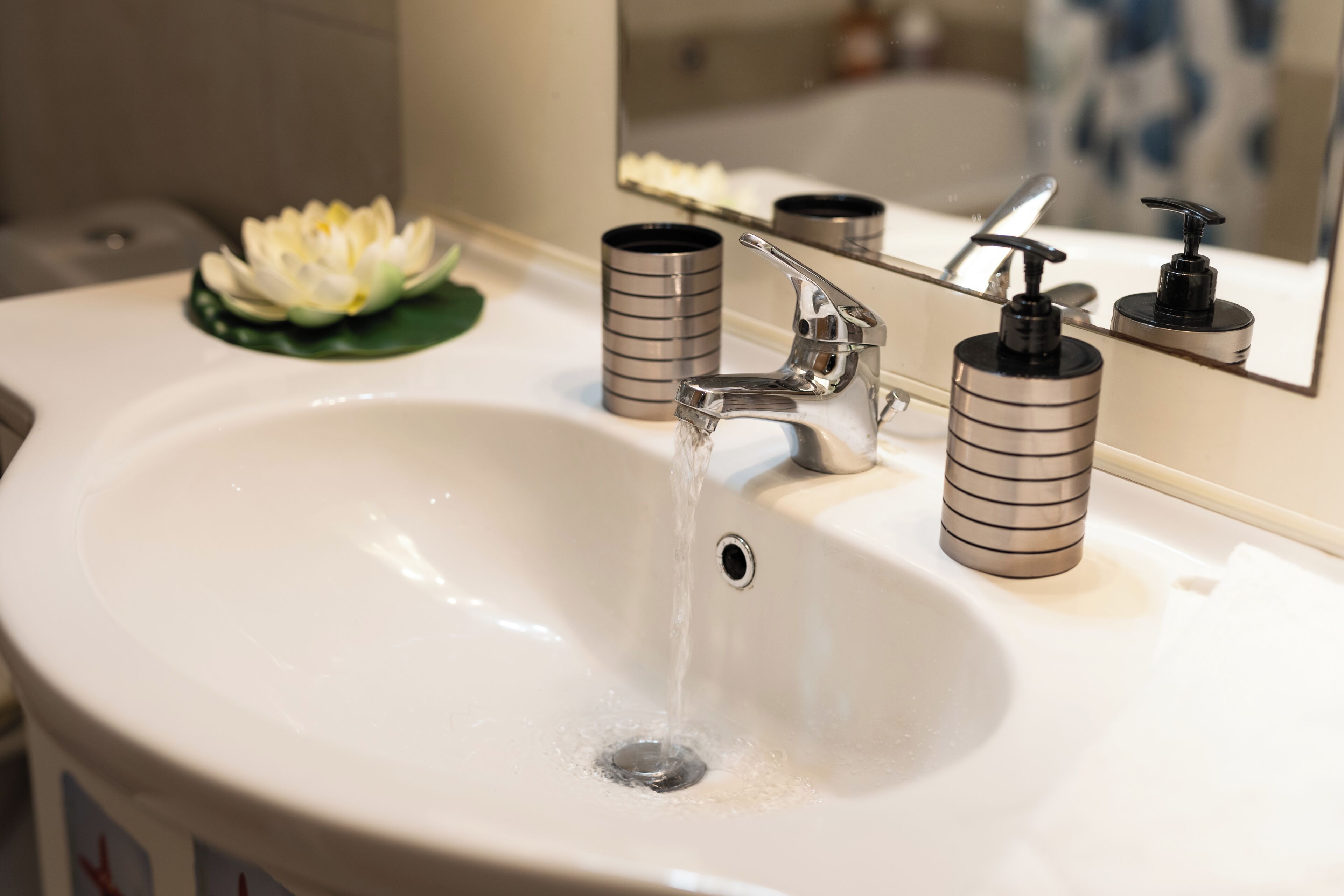 A bathroom sink with running water, a mirror, and two cylindrical containers.