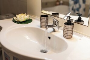 A bathroom sink with running water, a mirror, and two cylindrical containers. - Marias Cozy getaway in Glyfada (Glifada)