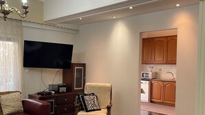Ein Wohnzimmer mit einer Couch, einem Couchtisch, einem Fernseher und einem Sessel mit Kissen.