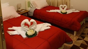 Ein Hotelzimmer mit zwei Betten, roter Bettwäsche, einer Handtuch-Herz-Dekoration, einer Klimaanlage, einem Nachttisch mit Lampe und einem gemusterten Boden.